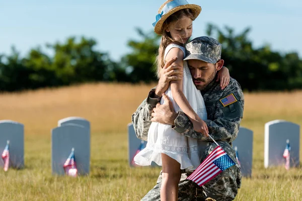 Military father in uniform hugging child near headstones in graveyard — Stock Photo