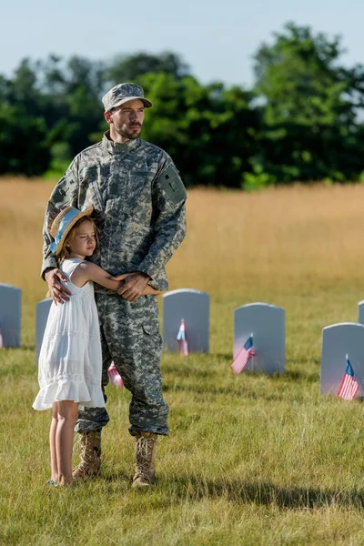 Padre militare in uniforme abbracciare figlia vicino lapidi nel cimitero — Foto stock