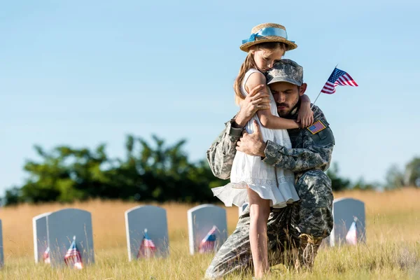 Uomo militare con gli occhi chiusi abbracciando figlia vicino lapidi nel cimitero — Foto stock