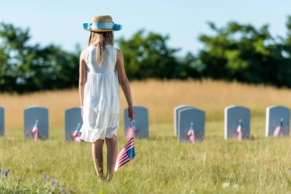 Back view of kid in white dress standing on graveyard with american flag — Stock Photo