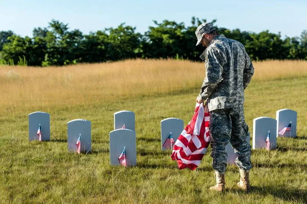 Military man in uniform holding american flag in graveyard — Stock Photo