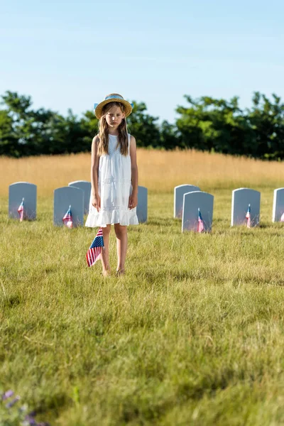 Selective focus of child in white dress standing on graveyard with american flag — Stock Photo