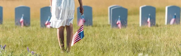 Panoramic shot of child in white dress standing on graveyard with american flag — Stock Photo