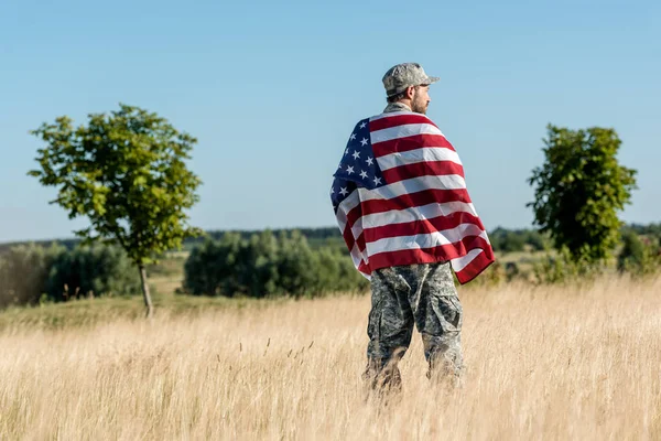 Homem de camuflagem uniforme segurando bandeira americana em campo dourado com árvores verdes — Fotografia de Stock