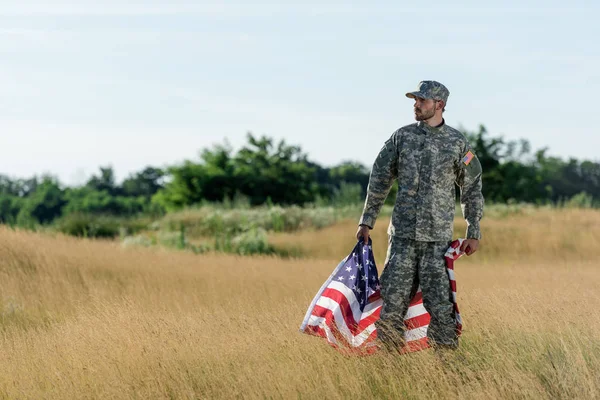 Soldat en uniforme de camouflage tenant le drapeau américain dans le champ d'or — Photo de stock