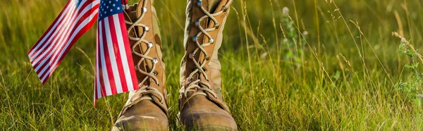 Panoramic shot of military boots near american flag with stars and stripes on grass — Stock Photo