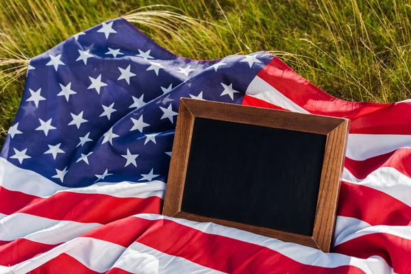 Empty chalkboard on american flag with stars and stripes on green grass — Stock Photo