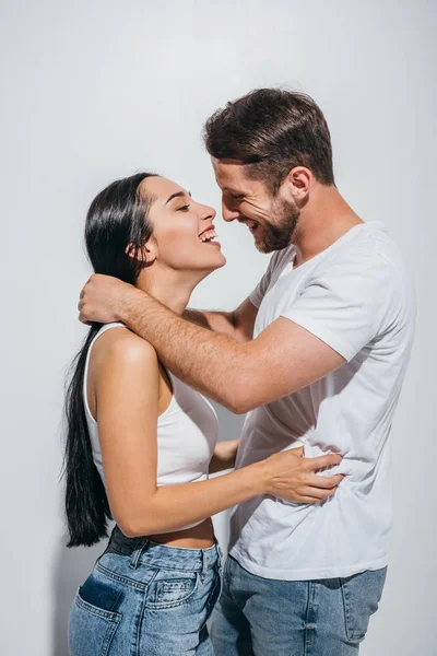 Vista lateral de la joven pareja abrazándose mientras sonríen y mirándose - foto de stock