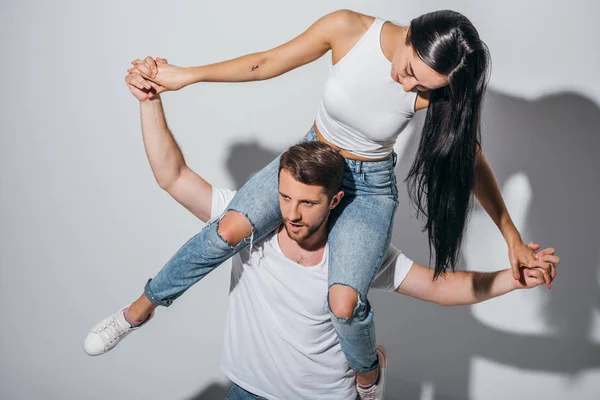 Jovem homem segurando namorada nos ombros enquanto sorrindo e de mãos dadas — Fotografia de Stock