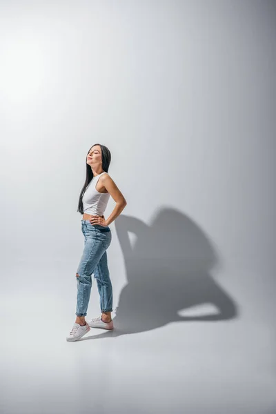 Full length view of beautiful girl standing in pose with hands on hips and closed eyes — Stock Photo