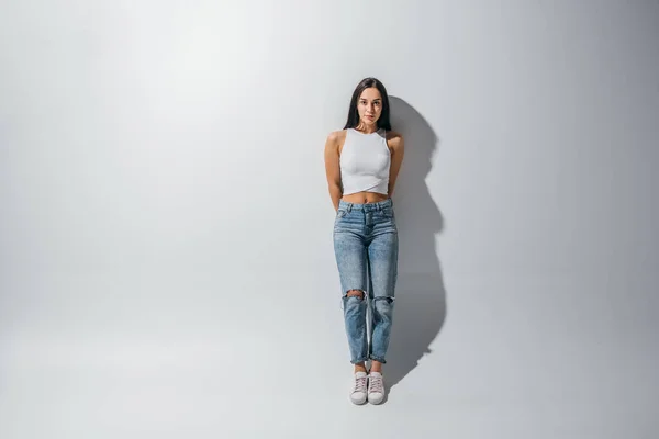 Full length view of beautiful girl standing near wall and looking at camera — Stock Photo