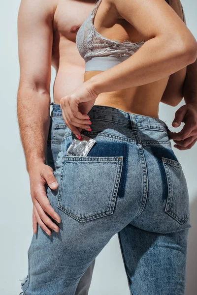 Recortado vista de chica posponer condón de jeans mientras de pie cerca de muscular hombre - foto de stock