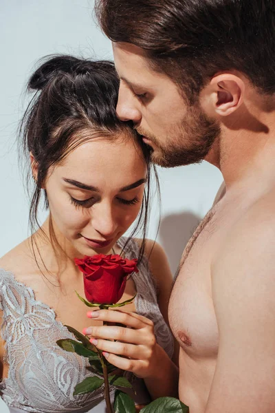 Handsome man kissing girlfriend in forehead while girl sniffing red rose — Stock Photo