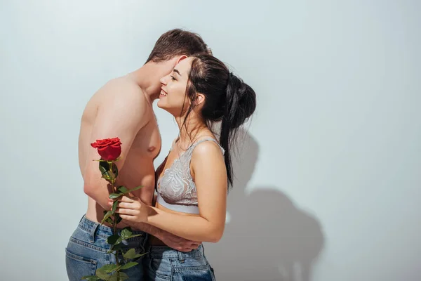 Вид збоку сексуальна пара обіймає і сміється, поки дівчина тримає троянду — стокове фото