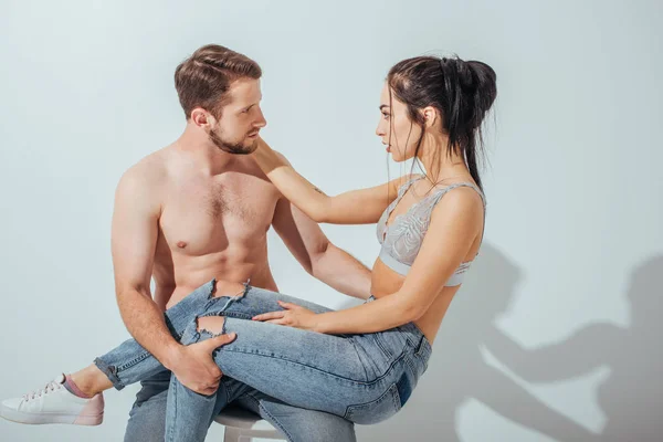 Sexy young couple looking at each other while girl sitting on knees of shirtless guy — Stock Photo