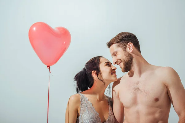 Shirtless couple smiling and looking at each other while girl holding red balloon — Stock Photo