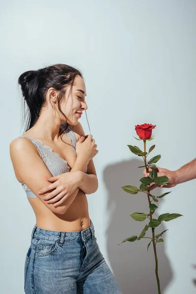 Обрізаний вид чоловіка, що дарує червону троянду сором'язливій дівчині, яка стоїть із закритими очима — Stock Photo
