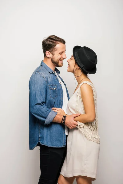 Vista lateral de la feliz pareja joven en ropa elegante abrazándose y mirándose - foto de stock