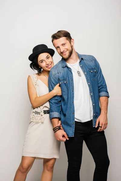 Jeune couple dans des vêtements élégants étreignant, souriant et regardant caméra — Photo de stock