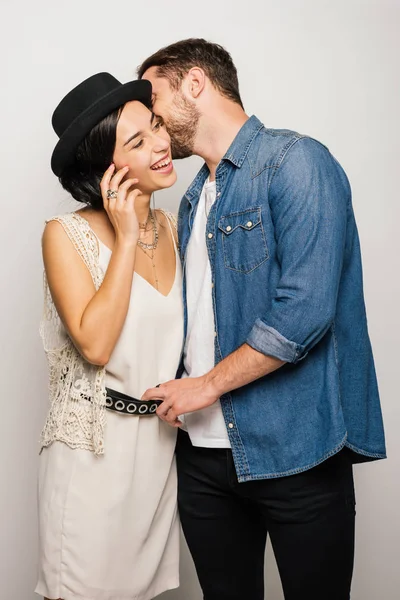 Beautiful girl in fashionable dress smiling while young man in stylish clothes whispering something into ear of girlfriend — Stock Photo