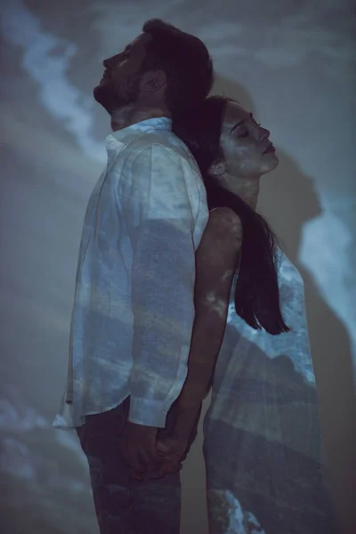 Вид сбоку мужчины и девушки, стоящие спиной друг к другу в темноте — стоковое фото
