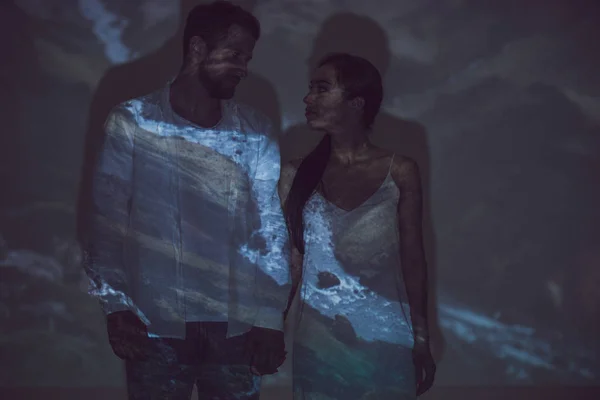 Couple standing in darkness, looking at each other and holding hands — Stock Photo