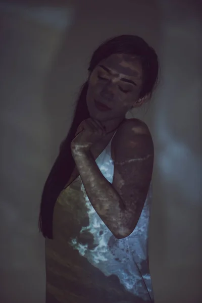 Красивая женщина, стоящая в темноте с закрытыми глазами и рукой у подбородка — стоковое фото