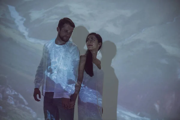 Couple in love holding hands and looking at each other while standing in dark place — Stock Photo