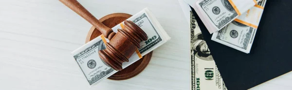 Tiro panorámico de billetes de dólar cerca del mazo del juez y carpeta en la mesa - foto de stock