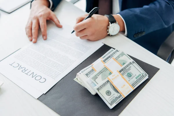Обрезанный взгляд бизнесмена, держащего ручку рядом с контрактом и деньгами в офисе — стоковое фото