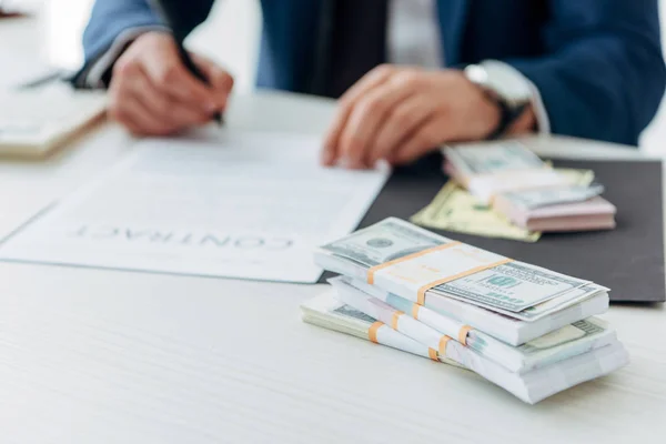 Selective focus of dollar banknotes near businessman signing contract in office — Stock Photo