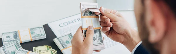 Panoramic shot of  businessman holding dollar banknotes near contract in office — Stock Photo