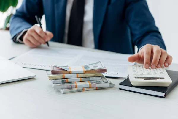 Обрезанный взгляд бизнесмена с помощью калькулятора рядом с деньгами и контрактом — стоковое фото