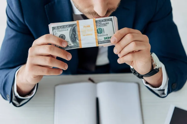 Vista cortada de homem cheirando notas de dólar perto de notebook e caneta — Fotografia de Stock