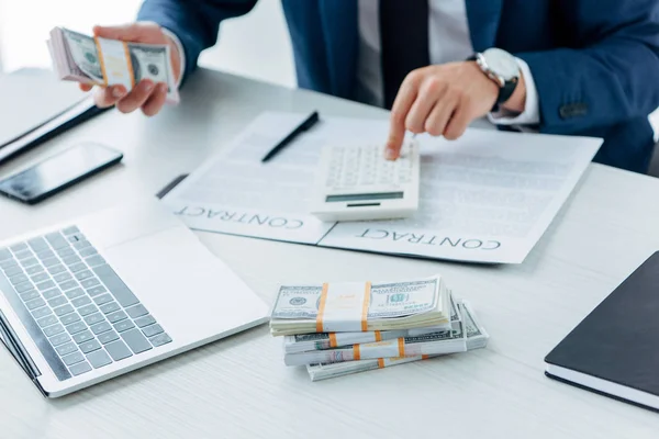 Cropped view of businessman using calculator and holding money near contract — Stock Photo