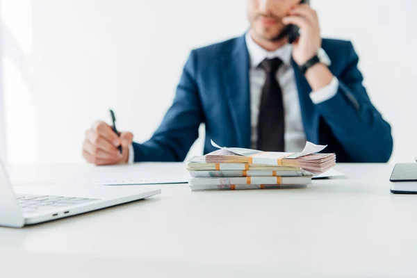 Selective focus of money near man talking on smartphone in office — Stock Photo