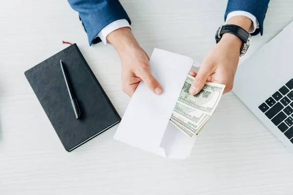 Vista superior del hombre de negocios sosteniendo sobre con billetes de dólar cerca del ordenador portátil - foto de stock