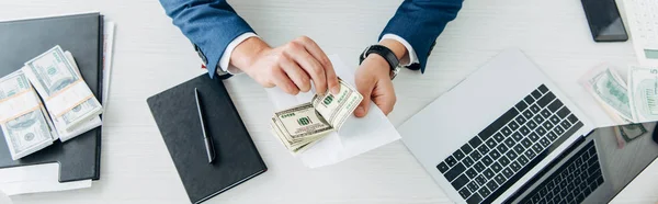 Panoramic shot of businessman holding bribe near notebook and pen on table — Stock Photo