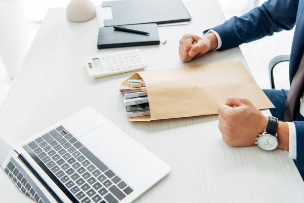 Ausgeschnittener Blick auf Geschäftsmann mit geballten Fäusten auf Tisch neben Umschlag mit Geld — Stockfoto