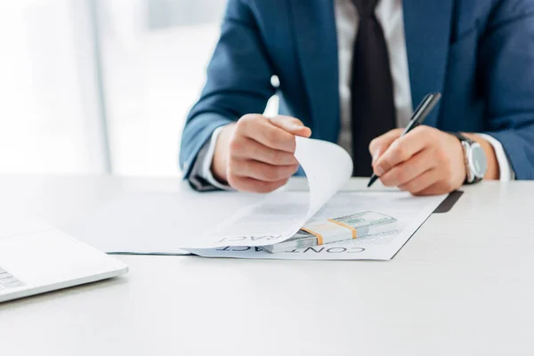 Cropped view of businessman holding pen and contract near bribe on table — Stock Photo