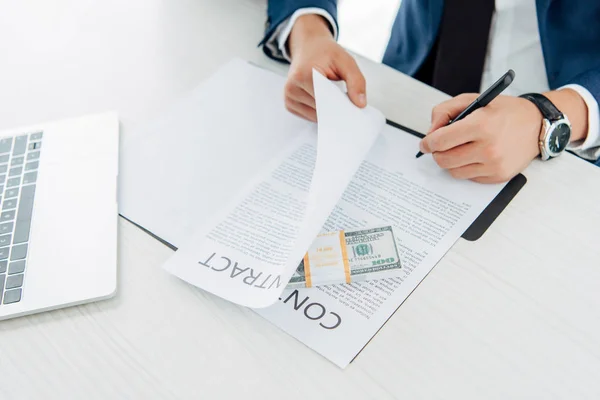 Верхний вид человека, держащего ручку при подписании контракта рядом с деньгами на столе — стоковое фото