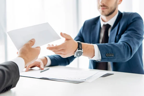 Cropped view of man giving envelope with bribe to business partner near table — Stock Photo