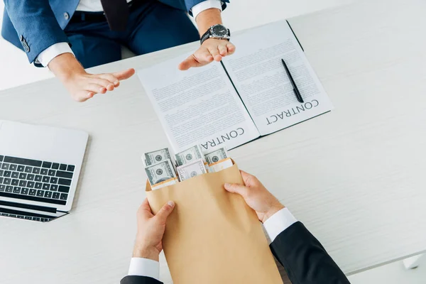 Vista superior del hombre haciendo gestos cerca de socio de negocios dando sobre con dinero en la oficina - foto de stock