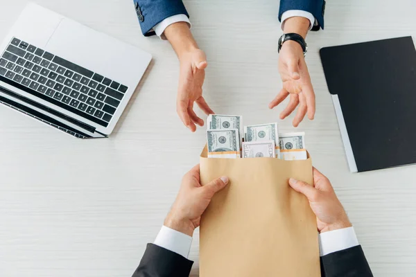 Top view of man taking envelope with cash near business partner and laptop — Stock Photo