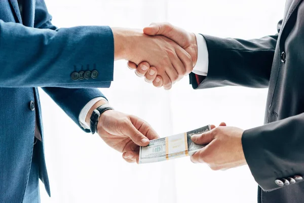 Visão cortada de empresário dando suborno ao parceiro de negócios e apertando as mãos sobre branco — Fotografia de Stock