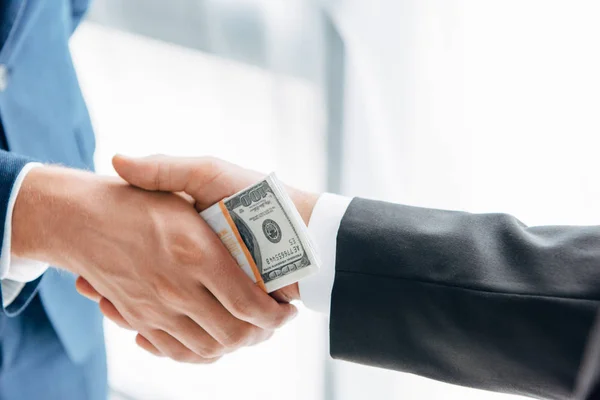 Cropped view of businessman giving bribe to business partner while shaking hands in office — Stock Photo