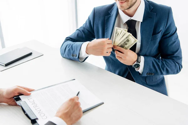 Vista recortada de la pluma de retención de hombre cerca del contrato y socio de negocios poniendo soborno en el bolsillo - foto de stock