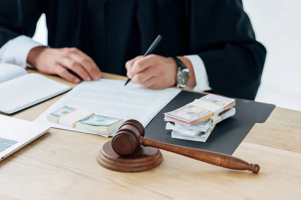 Cropped view of judge signing document near money and gavel — Stock Photo