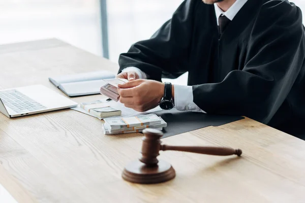 Selective focus of gavel near judge holding dollar banknotes in office — Stock Photo