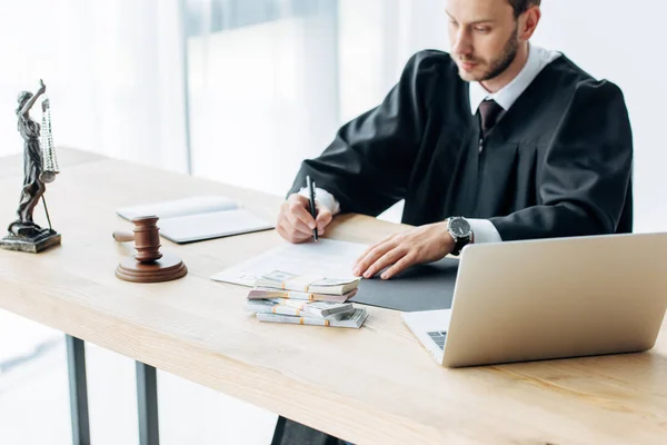 Selective focus of laptop near gavel and money near judge and money on table — Stock Photo